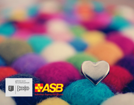 Diverse Wollknäuel in beige, dunkelblau, hellblau, gelb, pink, lila und rot. Auf einem Knäuel steckt ein silbernes Herz.